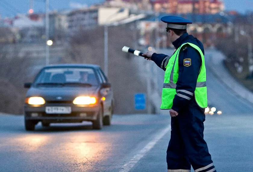 За поворотом стоит машина ГИБДД, рядом с ней сотрудник стоит с палочкой